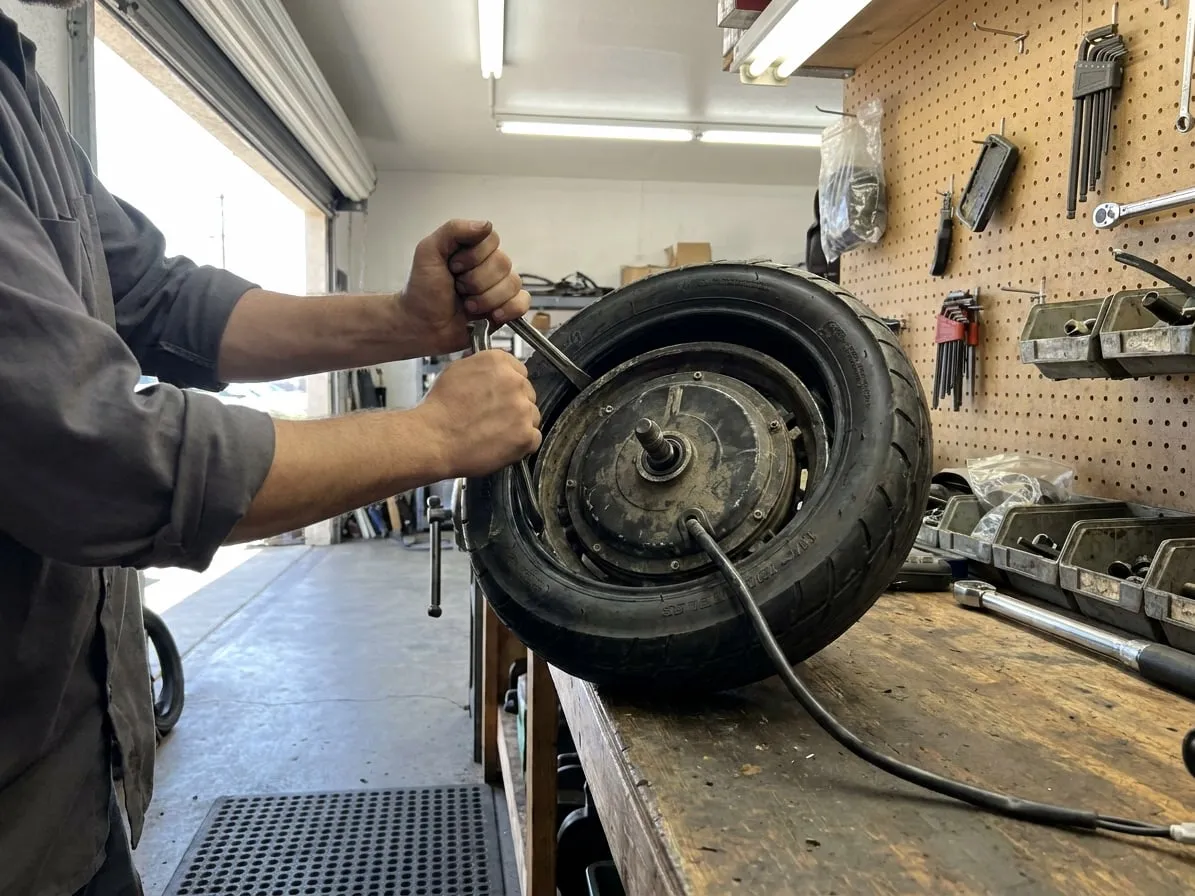 Technician fitting a new tubeless tire onto the hub-motor wheel of a heavy electric scooter